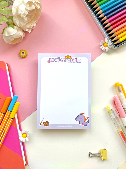 A6 notepad with a pastel purple background featuring Figment surrounded by art-themed doodles and the phrase “Keep Creating” — ideal for creative notes and planning.