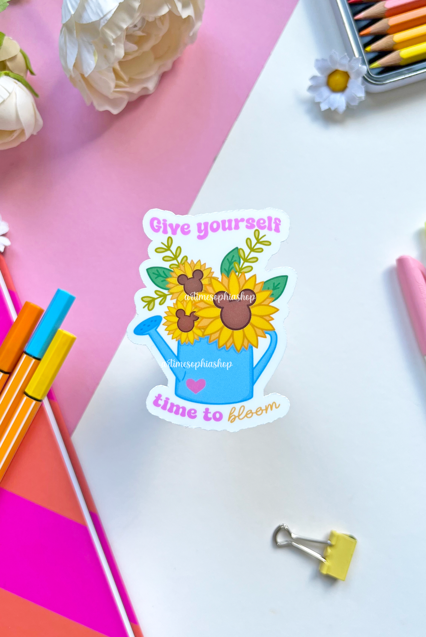 Vinyl sticker of a watering can filled with blooming sunflowers and the message “Give Yourself Time To Bloom” — a symbol of growth and self-care.