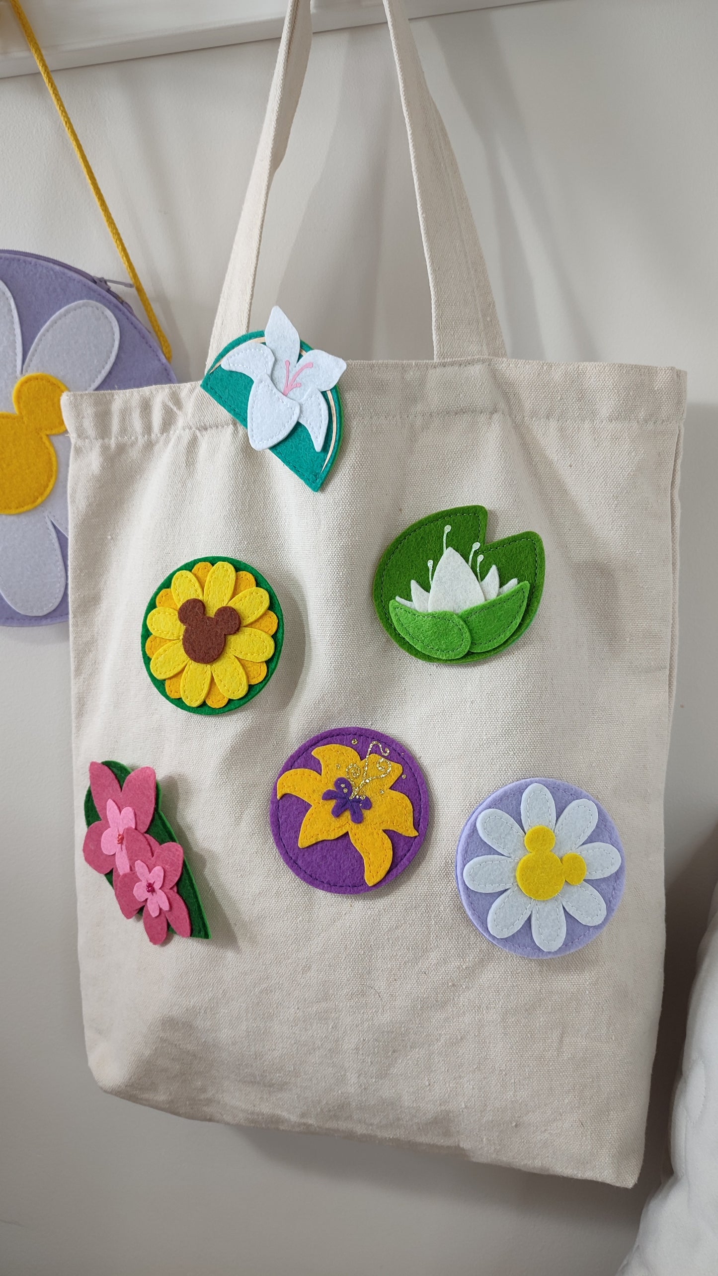 A collection of handmade felt flower accessories inspired by Disney characters — including Mulan’s magnolia, Rapunzel’s sun drop flower, Tiana’s lily pad, a sunflower, and a daisy. Shown styled as keychains, magnets, pins, and hair clips — perfect for Disney Bounds, gifts, or floral decor.